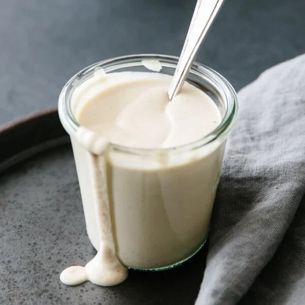 Vegan alfredo sauce in a glass jar with a spoon.