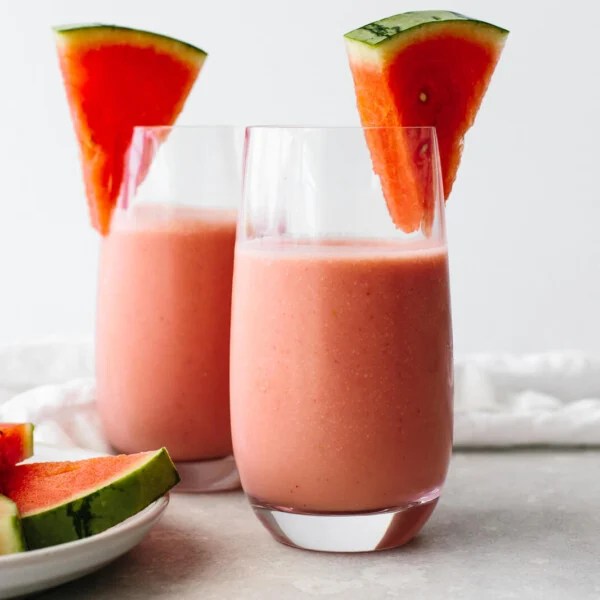 Two glasses of watermelon smoothie next to watermelon slices