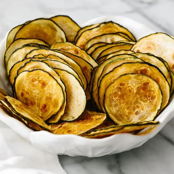 A white bowl holding thinly sliced zucchini chips layered on top of one another.