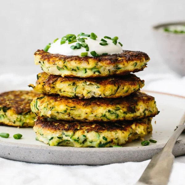 Four zucchini fritters on a plate, topped with sauce and chives.
