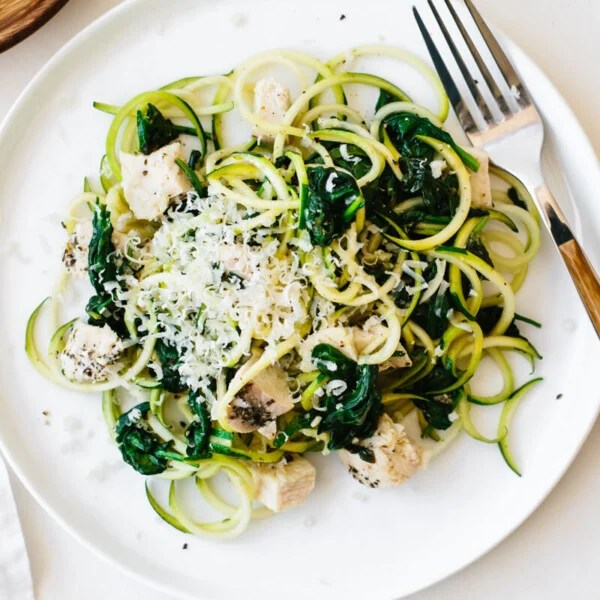 A plate of zucchini noodles with chicken, spinach and parmesan with a fork on the edge of the plate.